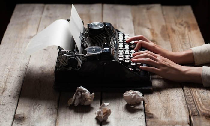 Hands writing on old typewriter over wooden table background