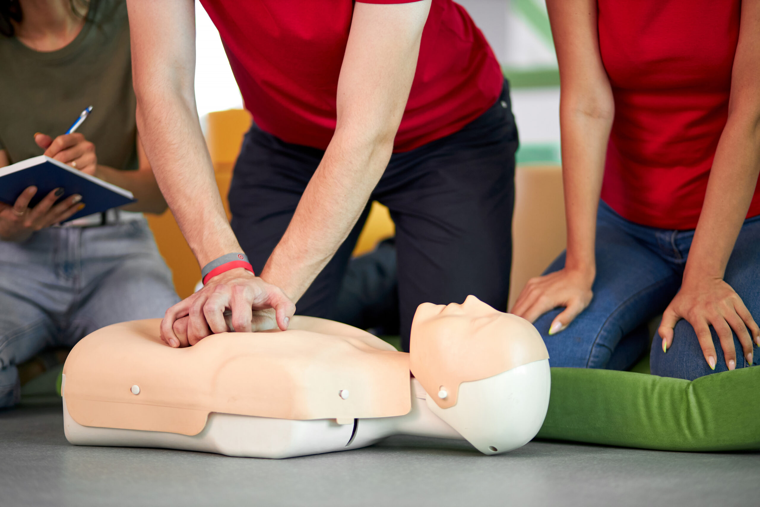 young male practicing CPR on a mannequin in the presence of people